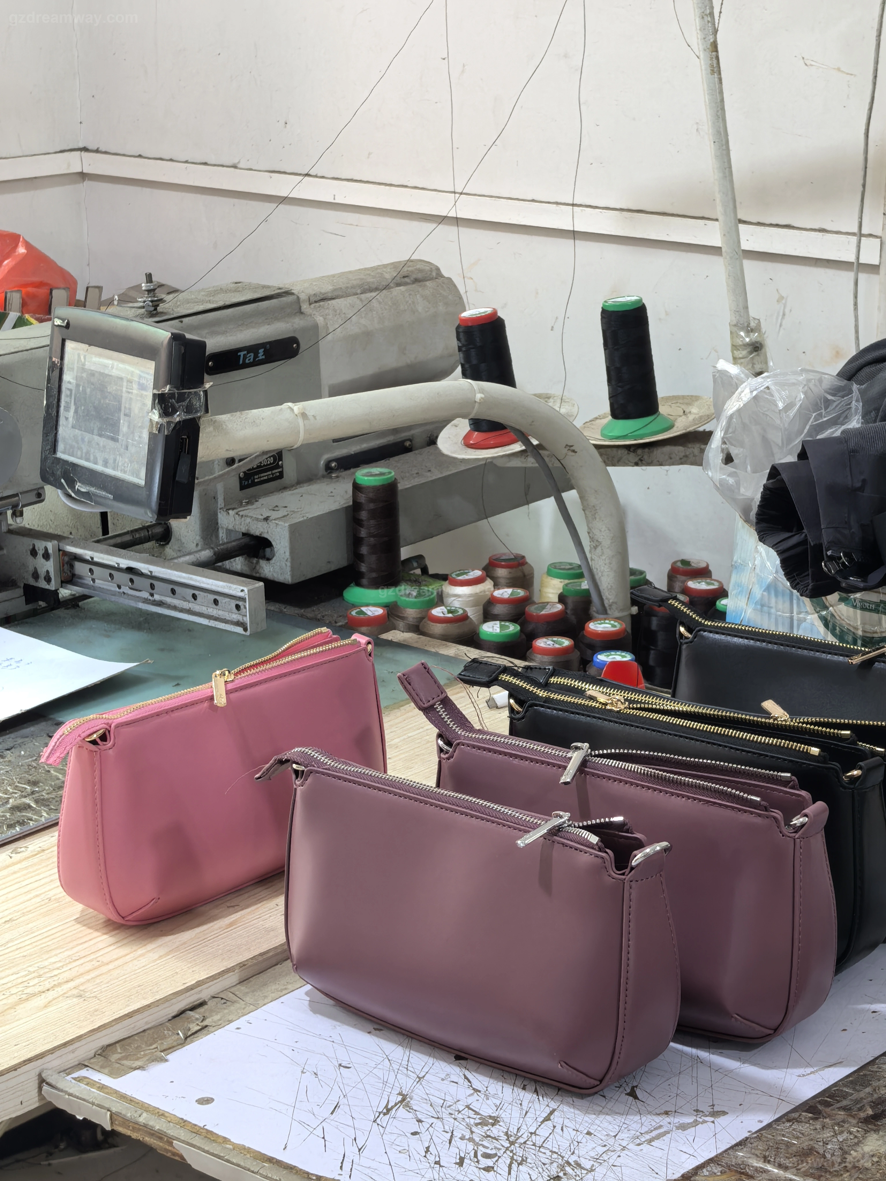 Sample handbags in pink, black and brown lined up beside a computerized template sewing machine used for OEM custom tote bag, leather backpack and branded canvas bag with logo production in Guangzhou workshop