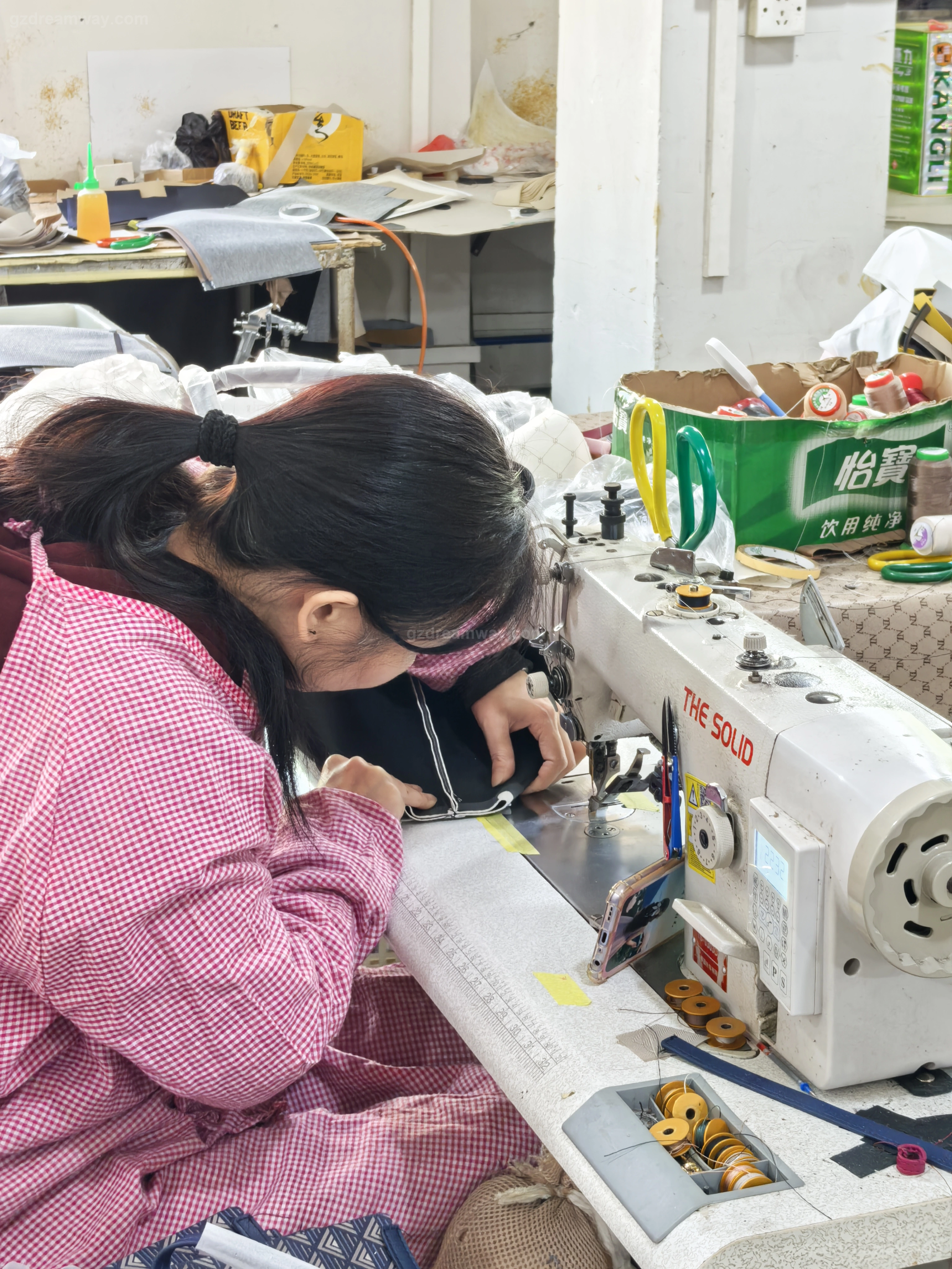 Experienced female operator using an industrial flat-bed sewing machine to attach zippers and binding to a custom canvas tote bag with logo inside GZ Dreamway Guangzhou bag factory production line