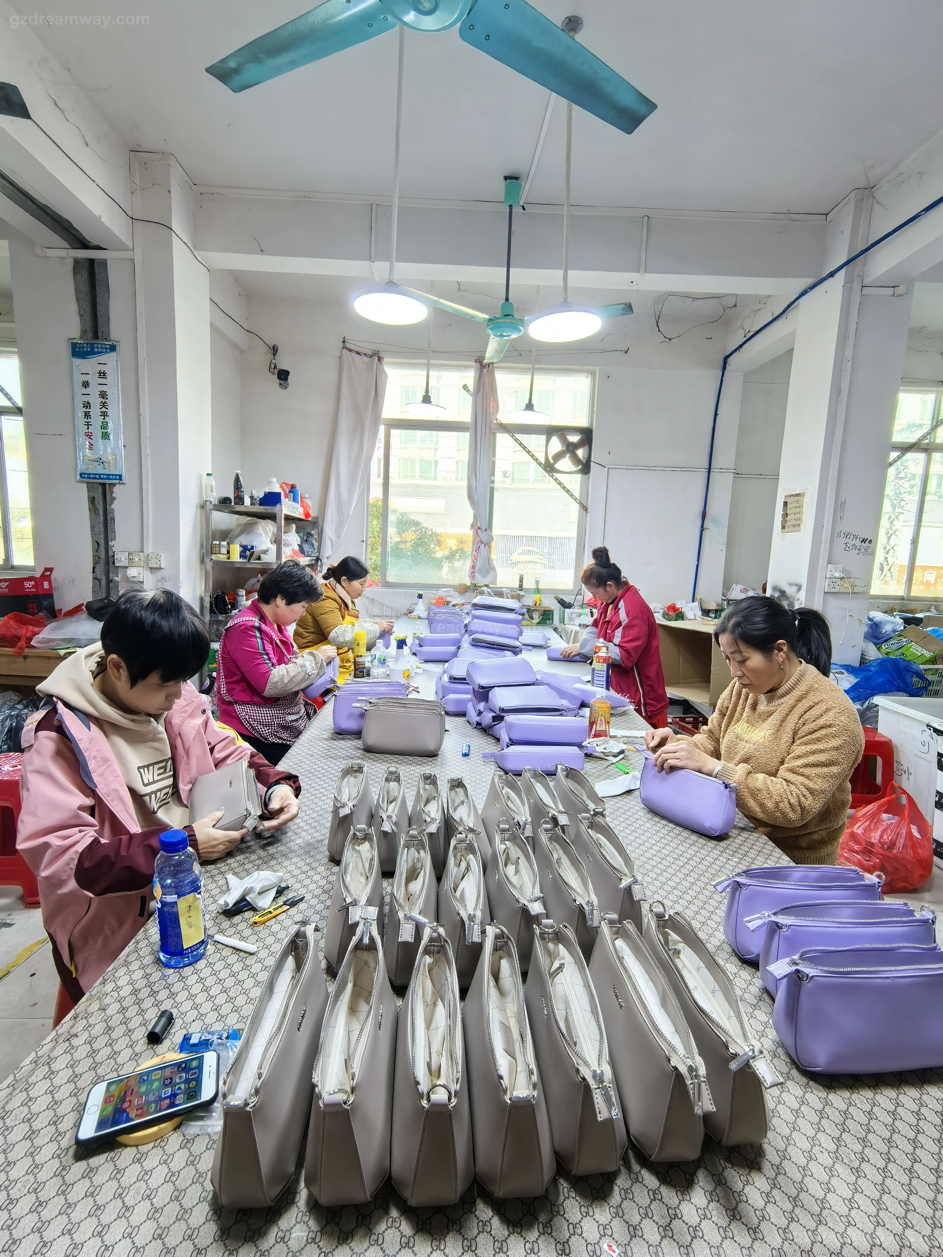 100 percent quality control line for underarm and crossbody bags in lavender purple and beige custom colors on long QC tables inside GZ Dreamway Guangzhou bag factory before export packing